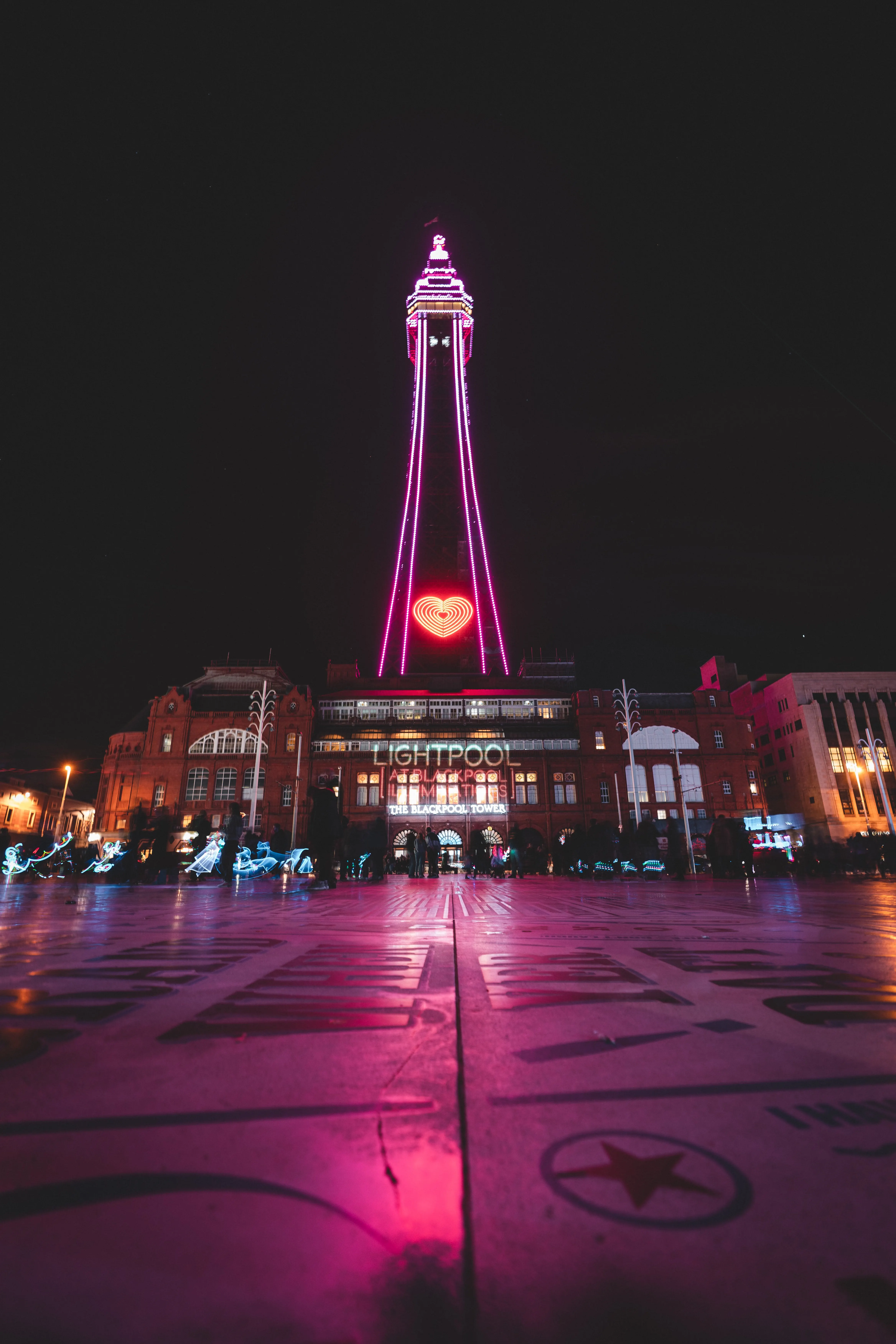 A ground level view of the Blackpool Tower lit up pink against a black sky